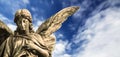 Guardian angel sculpture with open long wings isolated with blurred white clouds blue sky. Angel sad expression sculpture. Royalty Free Stock Photo