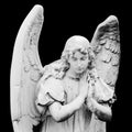 Guardian angel sculpture with open wings isolated on black background. Angel sad expression sculpture with eyes down and hands Royalty Free Stock Photo