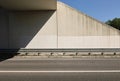 Guardrail in protection of sidewalk and concrete wall of an underpass . Two lane road in front.