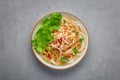 Guay Tiew Gai Cheek or Thai Chicken Noodle Soup in white bowl on gray concrete backdrop. Thai food