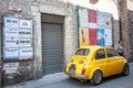 Old yellow small vintage car parked in old town street under wall of posters in Italian language Royalty Free Stock Photo