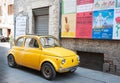 Old yellow small vintage car parked in old town street under wall of posters in Italian language Royalty Free Stock Photo