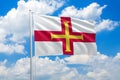 Guernsey national flag waving in the wind on clouds sky. High quality fabric. International relations concept