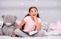 Guess her favorite fairy tale. Girl child sit bed with teddy bear read book. Kid prepare to go to bed. Pleasant time in