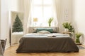 Guesthouse bedroom interior with a bed, bunches of wild flowers and an evergreen tree reflection in the mirror. Real photo.