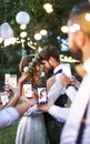 Guests with smartphones taking photo of bride and groom at wedding reception outside. Royalty Free Stock Photo