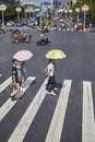 Women with sun umbrellas cross street in downtown Guilin.