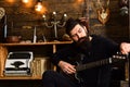 Guitar as hobby. Man bearded musician enjoy evening with bass guitar, wooden background. Guy in cozy warm atmosphere