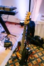 Guitar on a guitar stand in a musician`s room with a keyboard and LED heads in the background.