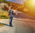 Guitar player hitchhiking on the edge of a country road at sunset Royalty Free Stock Photo