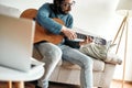 Guitar player. Young man playing guitar while sittting at home and watching video tutorial on laptop online. Distance Royalty Free Stock Photo