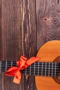 Guitar with red bow on wooden background.