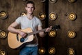 Guitarist, music. A young man plays an acoustic guitar on a background with lights behind him. Horizontal frame