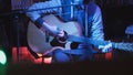 Guitarist plays acoustic guitar and sings microphone in night club, blue lights, close up