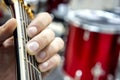 The guitarist`s hand, close-up and soft focus, takes the akrod on a guitar fretboard, against the background of the drum set. Royalty Free Stock Photo