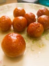 Gulab Jamun balls with sugar syrup placed in a white plate.