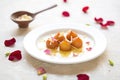 gulab jamun on white plate with rose petals