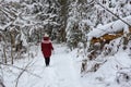 Woman wearing red winter jacket, walks in snowy forest.