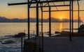 The sun dips below the mountains around in the Gulf of Palermo seen against the silhouette of a derelict boat hoist