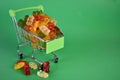 Gummy bears in a small supermarket cart on a green background.