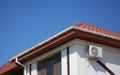 Guttering house. House building with plaster walls, window, red metal roof and white plastic roof gutter. Roofing construction.