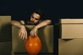 Guy with bare hands leans on boxes. Man with beard has rest on black background. Macho with tired face holds helmet