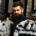 Guy with beard chooses furry coats. Rich fashion concept.