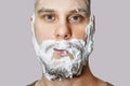 A guy with a beard with foam and gel on his face is preparing to shave in the morning at home on a colored background