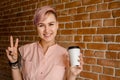 Young beautiful smiling girl holds paper cup of coffee on a brick wall background Royalty Free Stock Photo