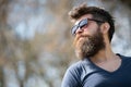 Guy with beard wears sunglasses. Hipster with beard and mustache on strict face, nature background, defocused. Man with Royalty Free Stock Photo