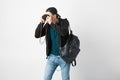 Guy with a black backpack on his shoulder dressed in a dark t-shirt, jeans, sweatshirt and a cap makes a photos in the Royalty Free Stock Photo