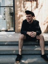 Guy in black cap laughing sitting on the stairs in sunlight. Vertical photo