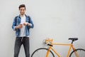 The guy in a blue denim jacket standing on wall background. young man near orange bicycle. Smiling student with bag Royalty Free Stock Photo