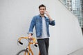 The guy in a blue denim jacket standing on wall background. young man near orange bicycle. Smiling student with bag Royalty Free Stock Photo