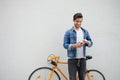 The guy in a blue denim jacket standing on wall background. young man near orange bicycle. Smiling student with bag Royalty Free Stock Photo