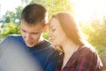 Guy in blue T-shirt and girl in plaid shirt are talking while sitting on bench in the park