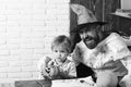 Guy and boy on white brick background. Man in orange hat and kid with happy, interested faces