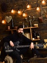 Guy in cozy warm atmosphere play relaxing soul music. Favourite activity. Man with beard holds black electric guitar Royalty Free Stock Photo