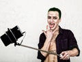 Guy with crazy joker face, green hair and idiotic smile. carnaval costume. making selfy photo