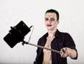 Guy with crazy joker face, green hair and idiotic smile. carnaval costume. making selfy photo