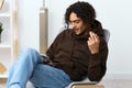 guy with curly hair sitting on a chair with a phone communication interior background