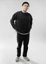 Guy dancer dressed in black jeans, sweatshirt, hat and gray sneakers stands in the studio on the white background