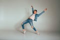 the guy dances on a white background in torn jeans, a white tank top and a denim jacket, hands are raised up, jump, pose