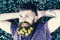 Guy with dandelions in beard relaxing, top view. Man with beard on smiling face put hands behind head. Breeziness Royalty Free Stock Photo