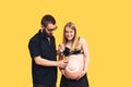 the guy draws with cream emoji on the belly of his pregnant wife on a yellow background