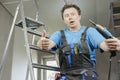 Guy in work clothes and with an electric screwdriver in his hand is standing on the stairs. Against the background of renovation Royalty Free Stock Photo