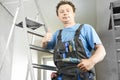 Guy in work clothes and with an electric screwdriver in his hand is standing on the stairs. Against the background of renovation Royalty Free Stock Photo