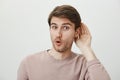 Guy enjoys put hit nose in business of other people. Thrilled handsome male holding palm near ear and saying wow Royalty Free Stock Photo