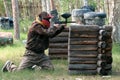 Landfill in the forest for a team game in paintball. A guy or girl in camouflage clothes peeks out from behind a wooden shelter wi Royalty Free Stock Photo