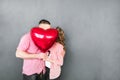 A guy and a girl hug and kiss hiding behind a balloon in the form of a heart